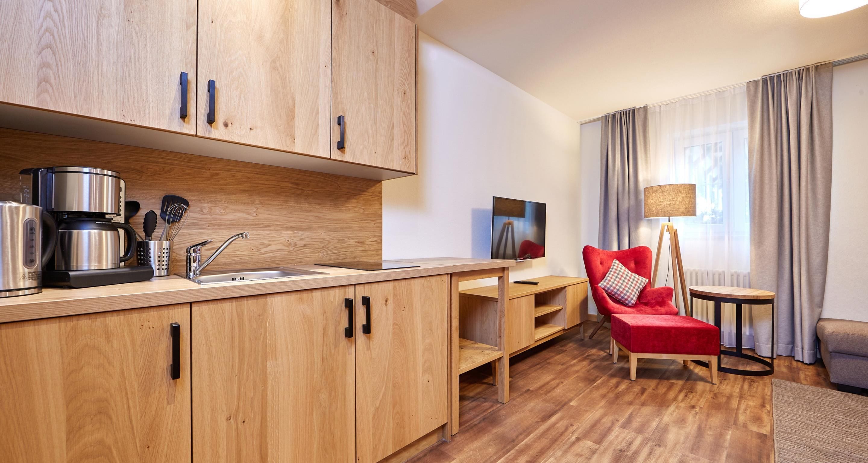 A modern kitchen with wooden cabinets and a built-in coffee maker. There is a dining area with a red chair and a small table.