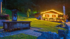 Un acogedor refugio con fachada iluminada, un banco de madera y un sendero de piedra que lleva a la entrada.