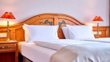 A double bed with white linens and a wooden headboard with a bow design. There are two bedside tables with lamps.