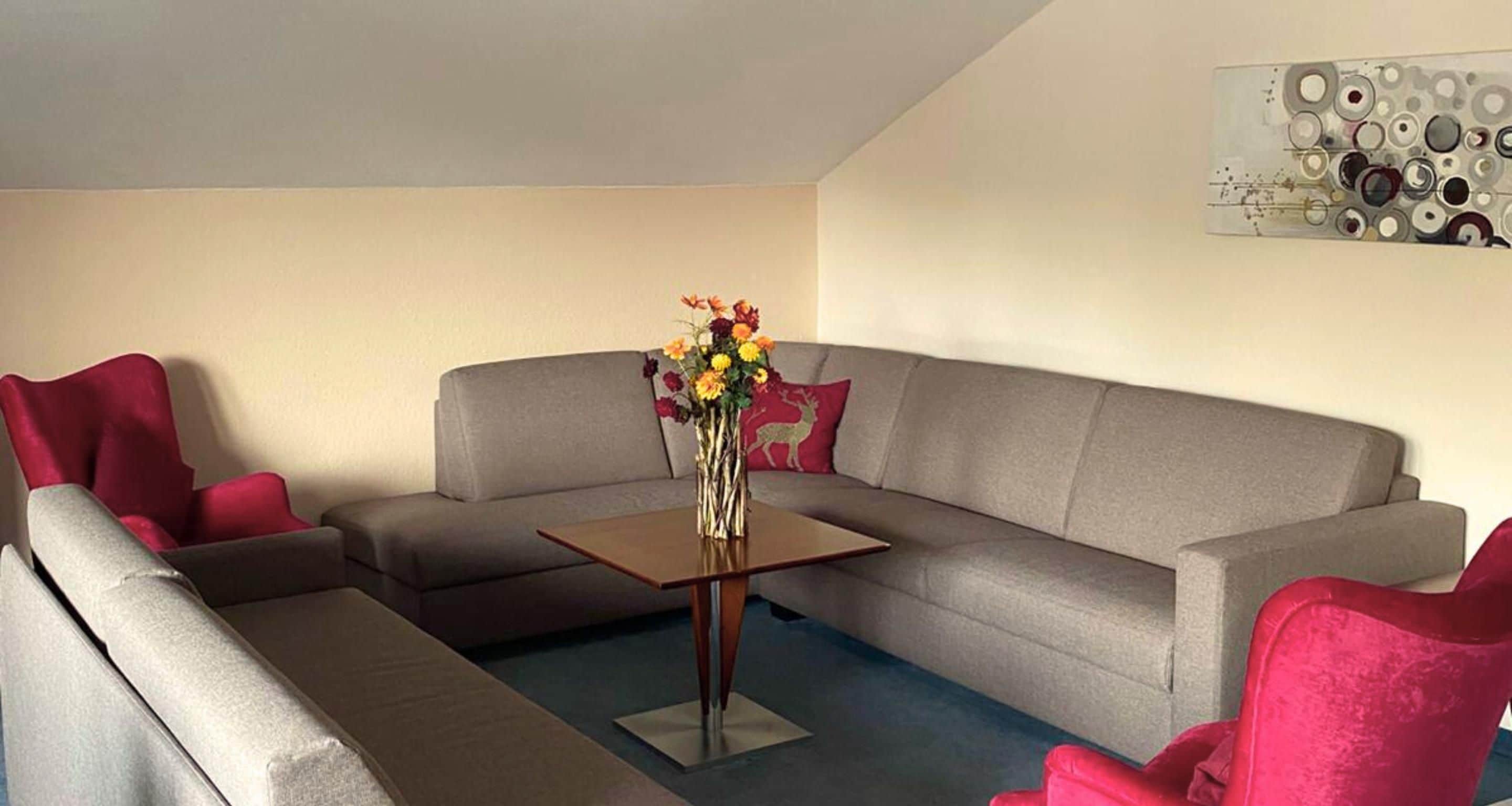 Una sala de estar con un sofá gris, una mesita de madera y un jarrón con flores.