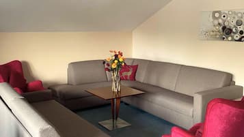 Una sala de estar con un sofá gris, una mesita de madera y un jarrón con flores.