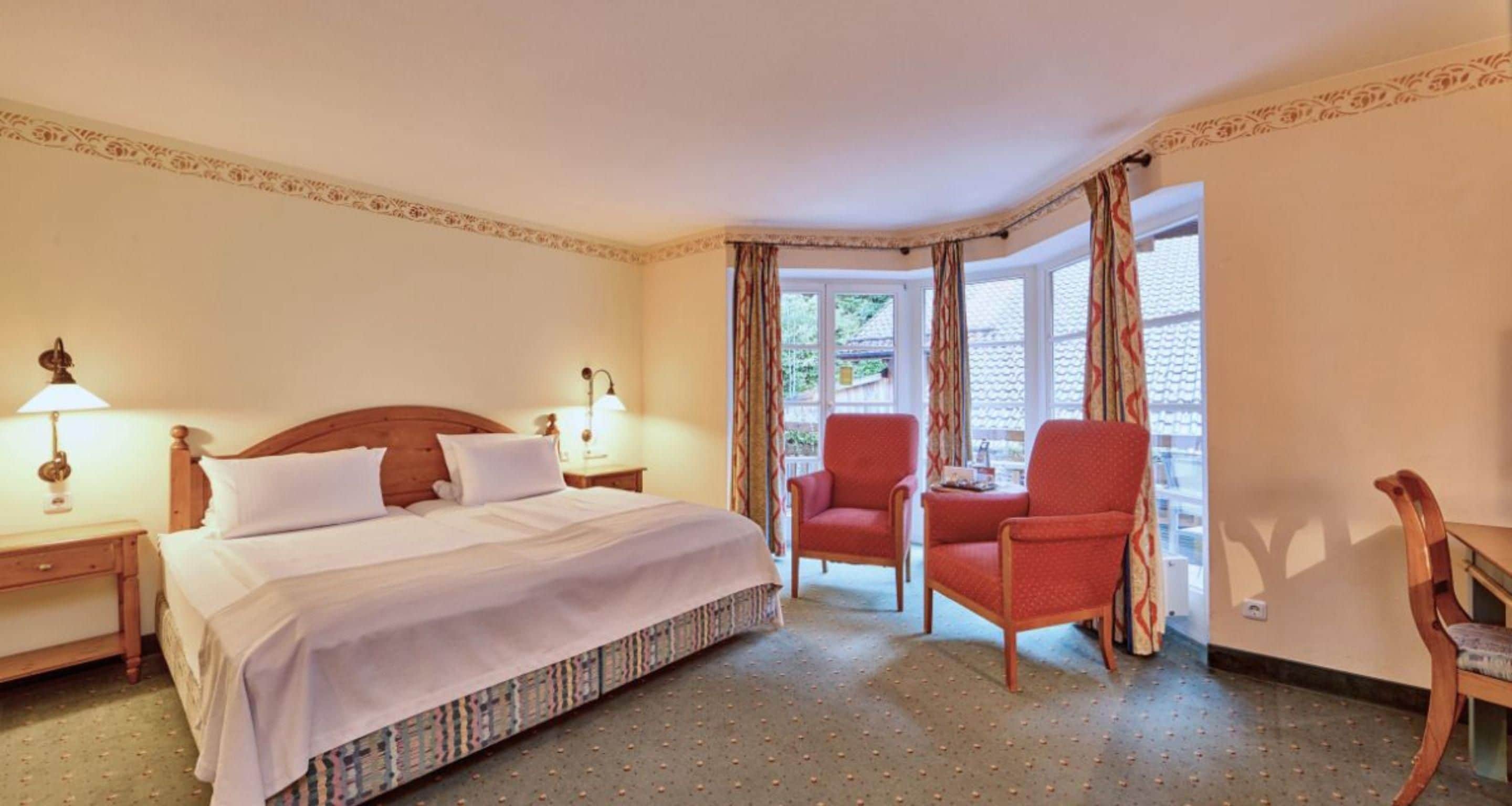 Een hotelkamer met een bed, twee nachtkastjes, een houten stoel en een raam met gordijnen.