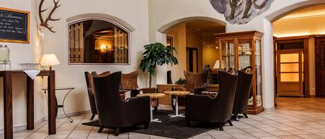 A lobby with a reception desk, a mirror, a chandelier, leather armchairs, and a large plant.