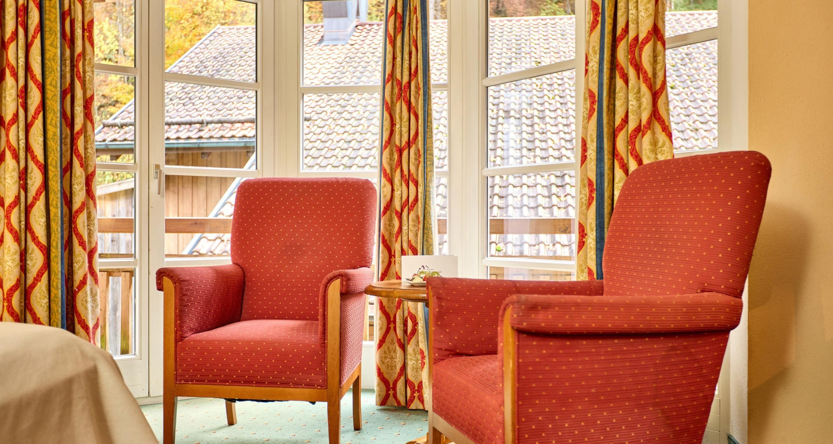 Una habitación con dos sillas rojas, una mesita y una ventana con cortinas estampadas.
