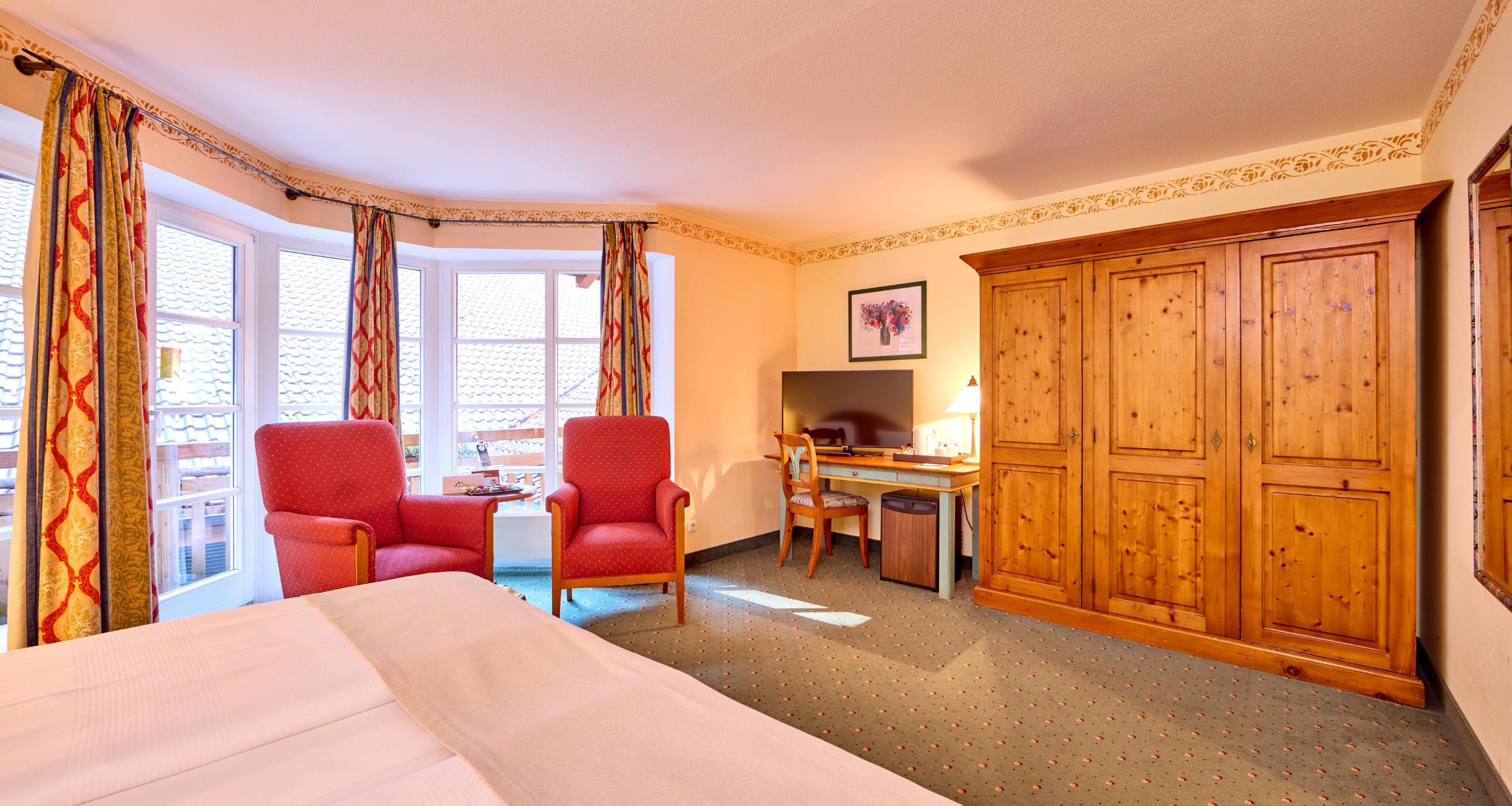 Une chambre d’hôtel avec un lit, deux chaises rouges, un bureau avec un ordinateur et une armoire.