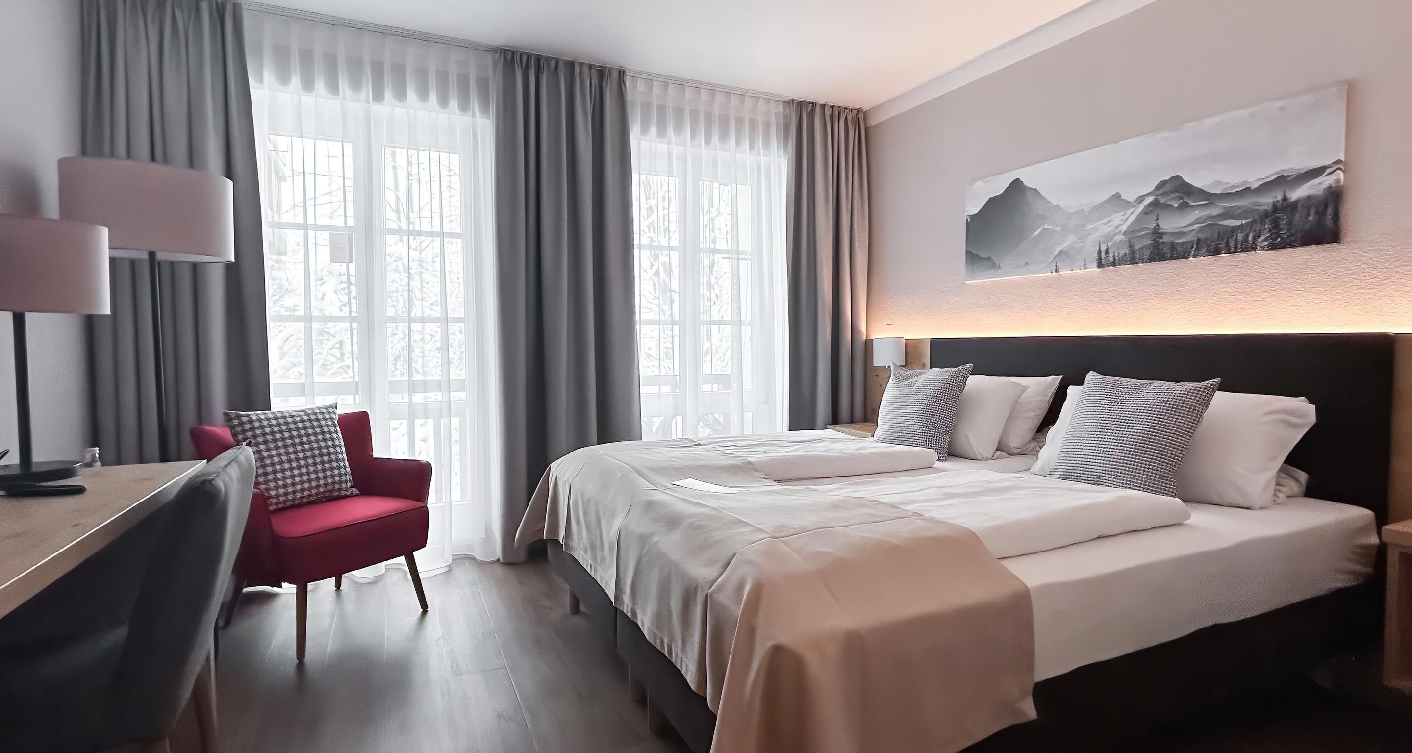 Ein Hotelzimmer mit einem Bett, einem Schreibtisch mit Stuhl, einer Lampe und einem Bild an der Wand.
