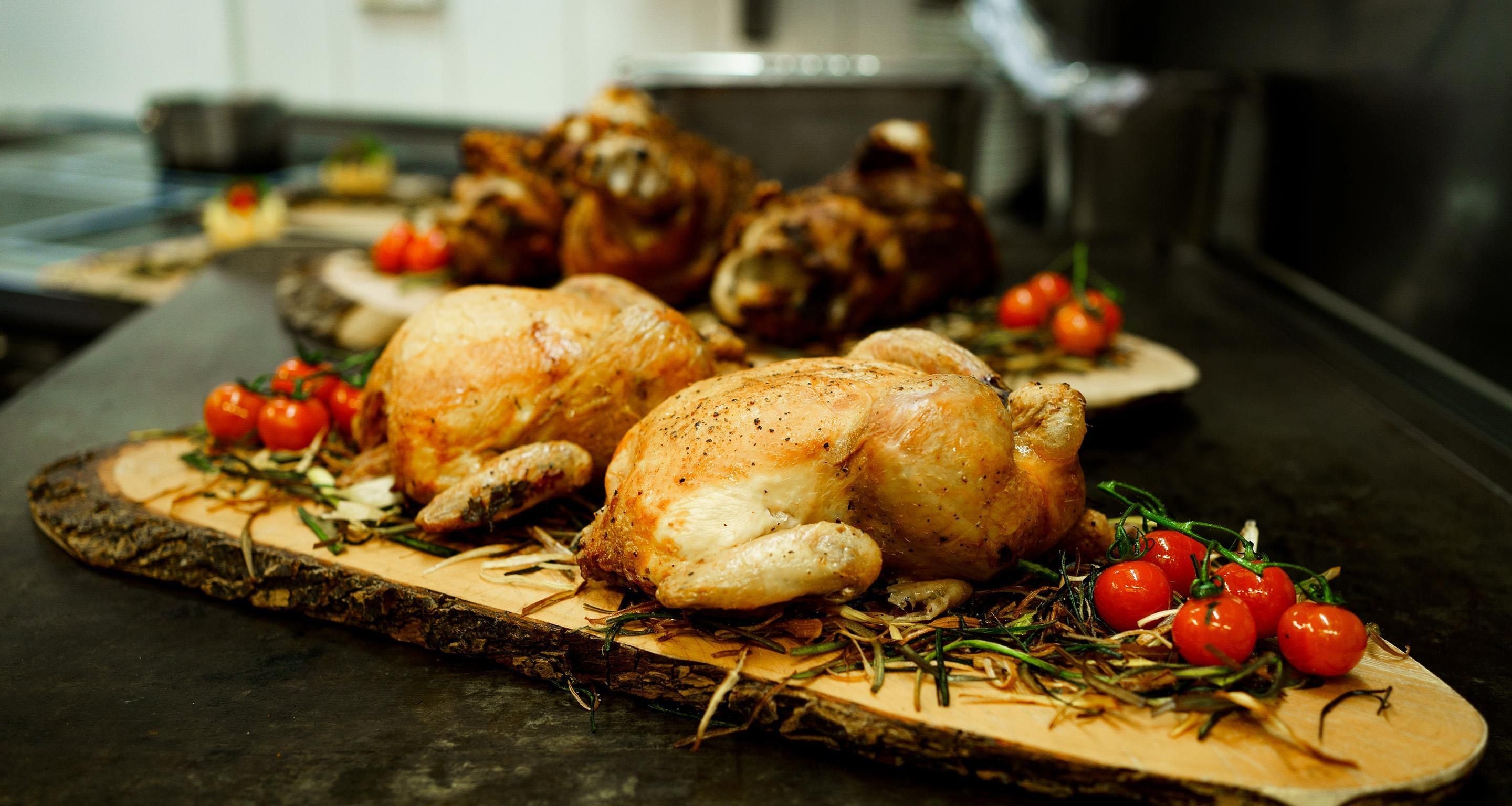 Roasted chicken with herbs and cherry tomatoes on a wooden board.