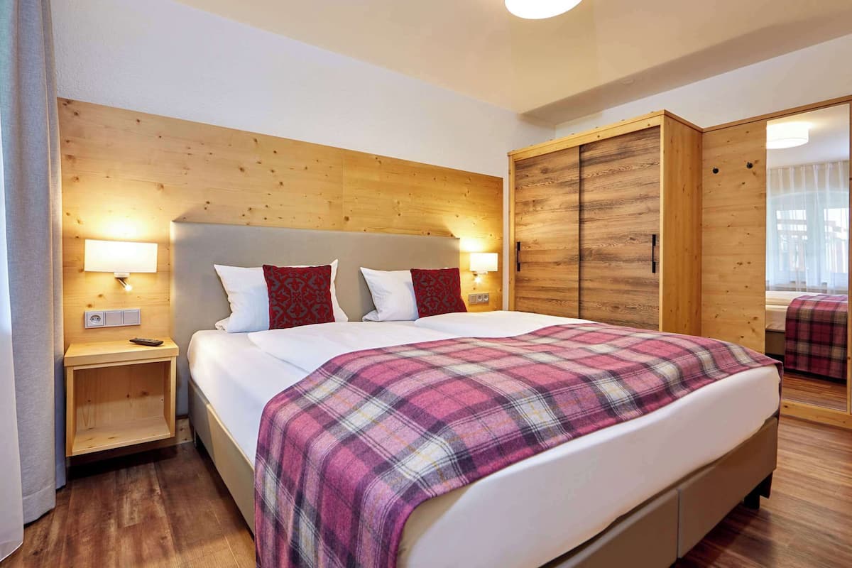 Quarto com cabeceira de madeira, cama com manta xadrez, luminárias de cabeceira e um guarda-roupa.