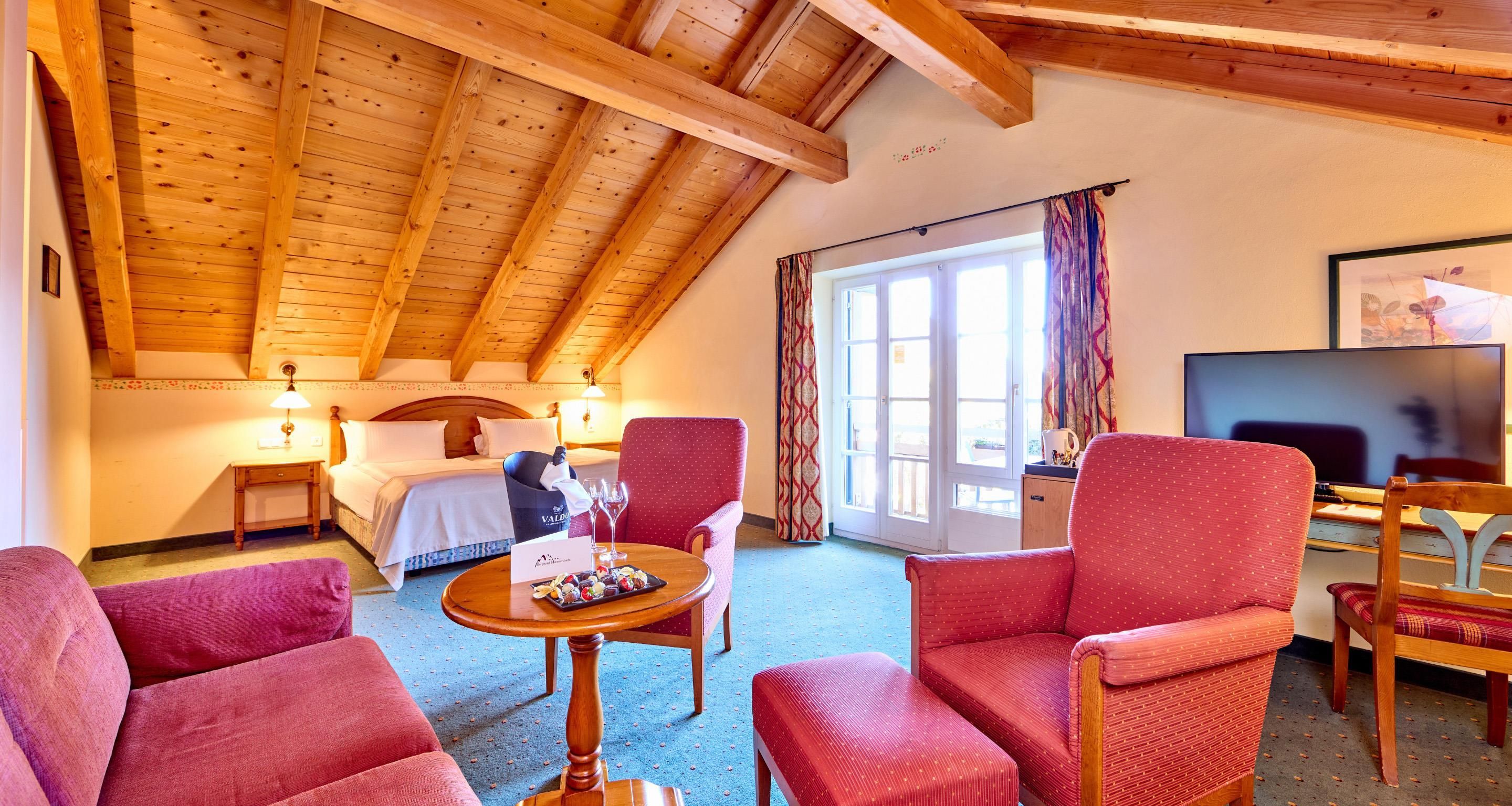 Hotelkamer met houten plafond, een bed, bureau met stoel, televisie en een eettafel met stoelen.