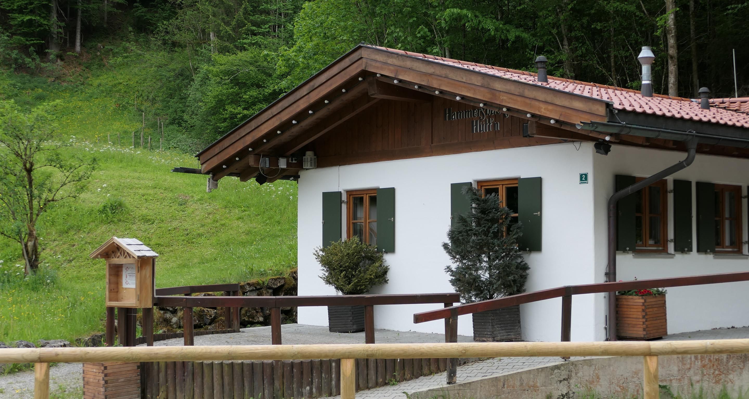 Un bâtiment à deux étages, doté d’une façade en bois et de volets verts, situé sur une colline, avec une clôture en bois en premier plan.
