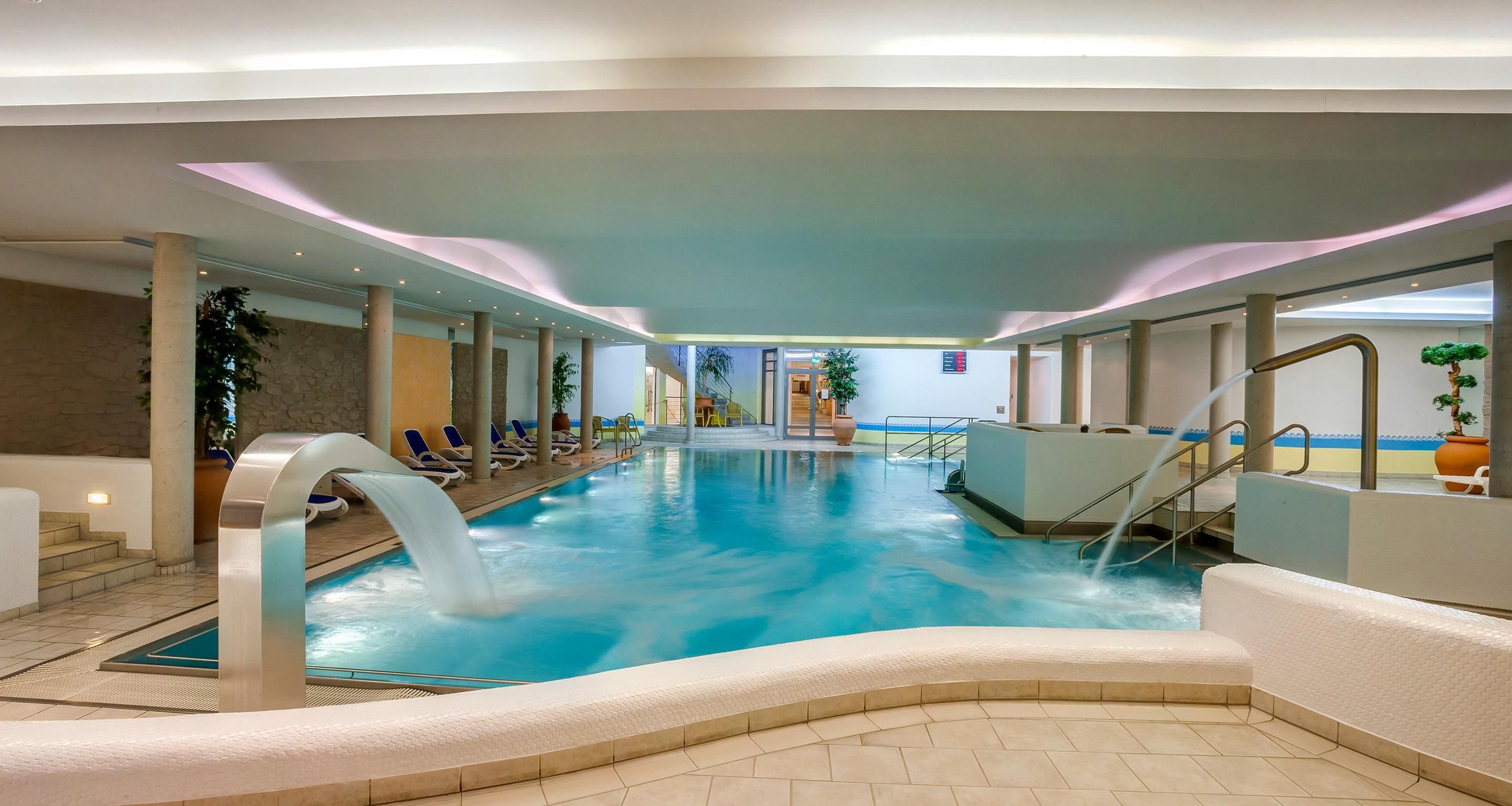 An indoor swimming pool with lounge chairs and a water slide.