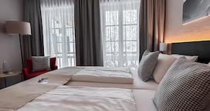 A hotel room with a large bed, a nightstand, a chair, and a window with curtains. - Berghotel Hammersbach, Sure Hotel Collection by Best Western (Grainau)