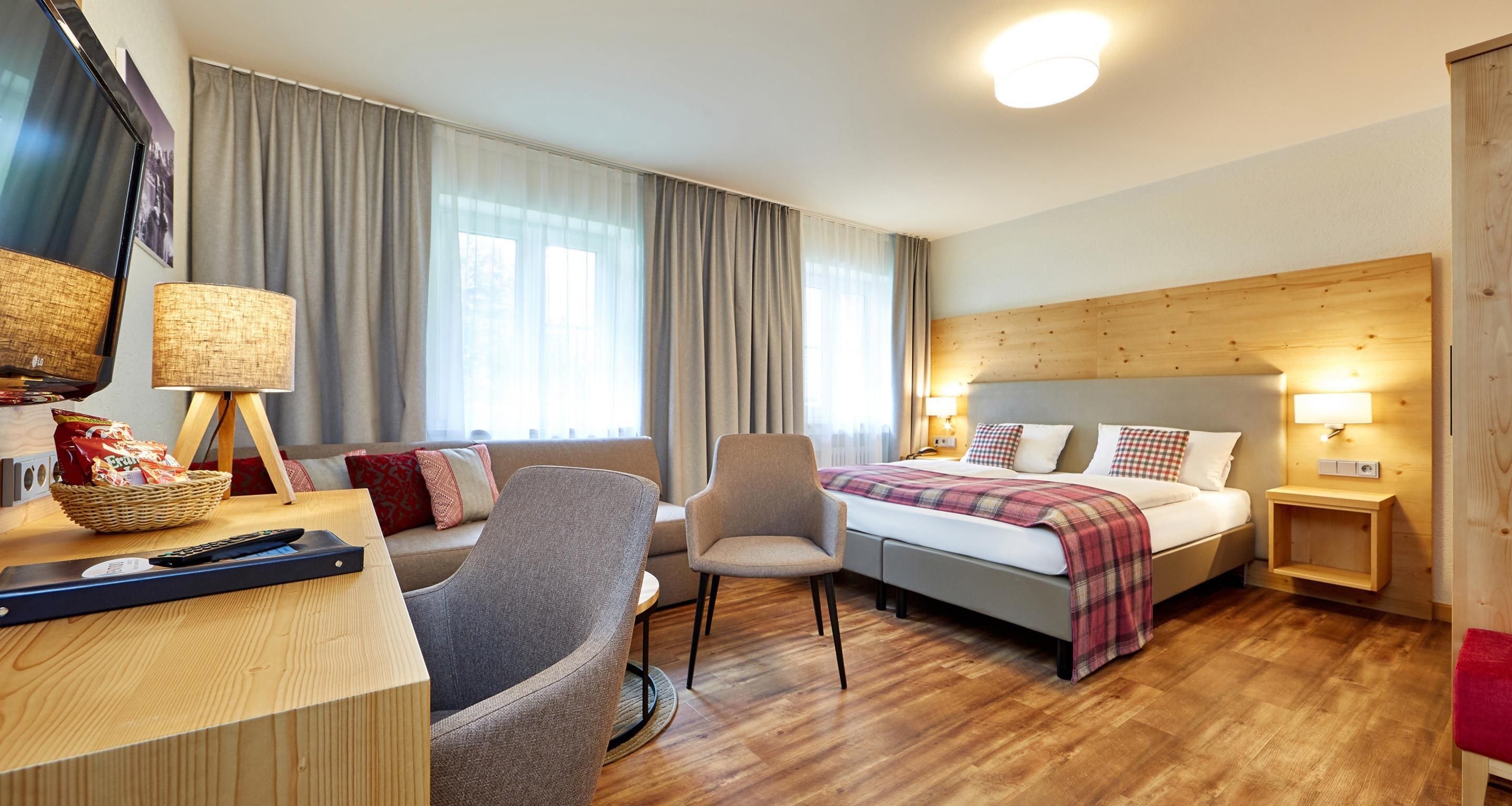 A hotel room with a bed, a desk with a lamp, a chair, and a television.