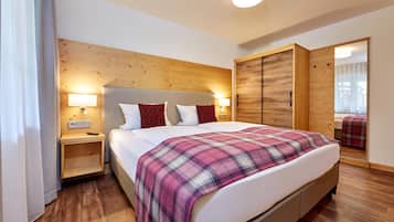 A hotel room with a wooden headboard, a bed with a plaid blanket, bedside lamps, and a wardrobe with a mirror.