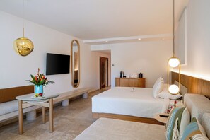 A modern hotel room with a bed, bedside table, a small round table with a vase of flowers, a large mirror, and a flat-screen TV mounted on the wall. - Kimpton Tres Rios All Inclusive by IHG (Playa del Carmen)