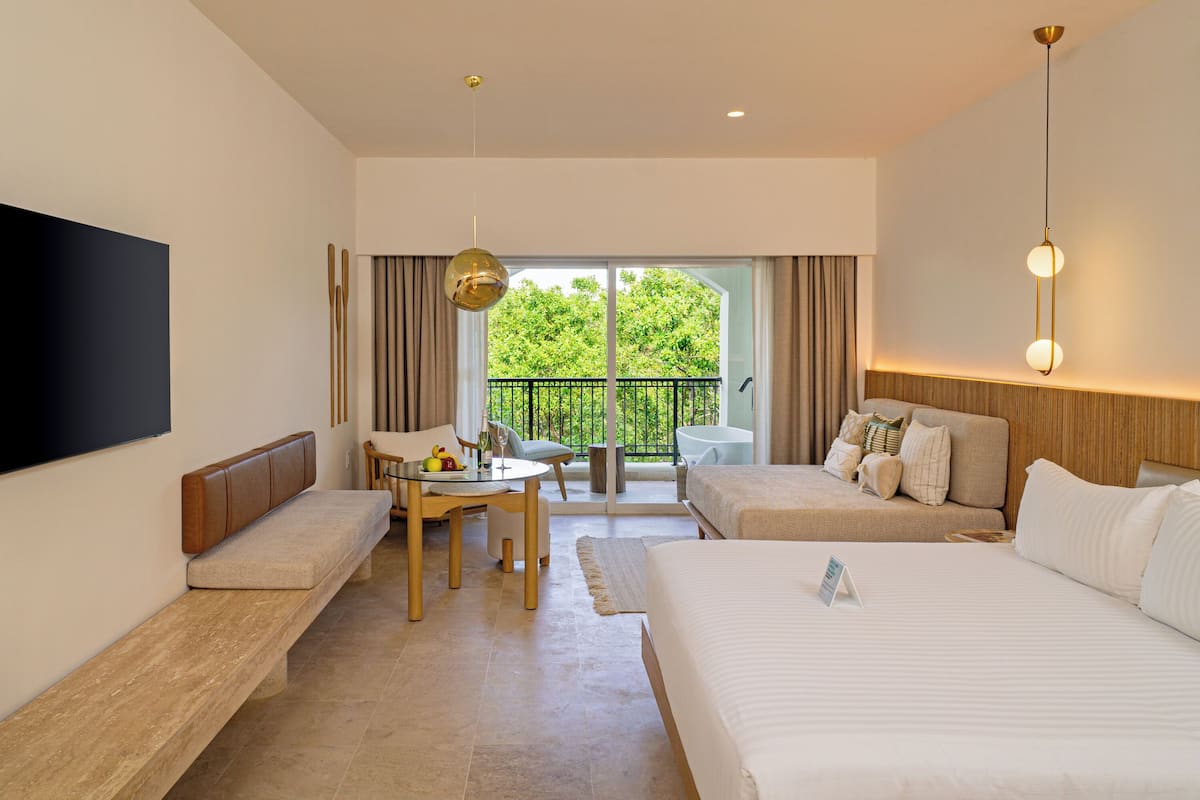 A hotel room with a large bed, a sofa, a dining table, and a TV.