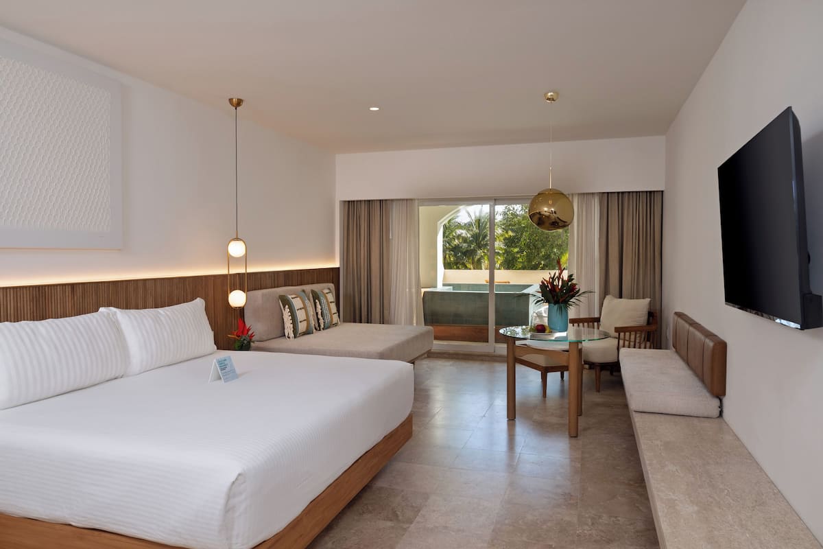 A hotel room with a large bed, a sofa, a dining table, and a TV.