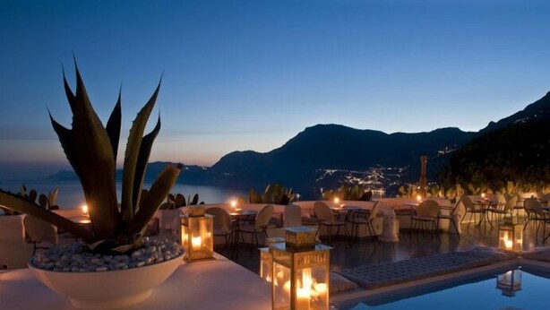 A serene evening setting with a pool, dining area, and mountain views. - Hotel Le Fioriere (Praiano)