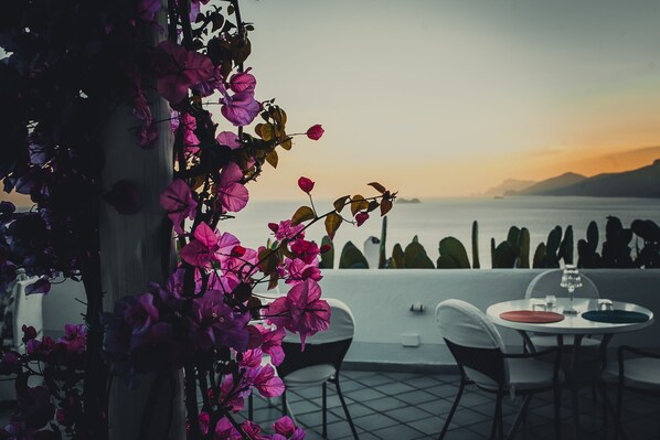 A terrace with a table and chairs, overlooking a body of water and mountains. - Hotel Le Fioriere (Praiano)