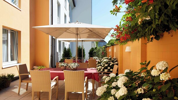 An outdoor patio with a table and chairs, surrounded by potted plants and flowers. - Best Western Hotel Lippstadt (Lippstadt)