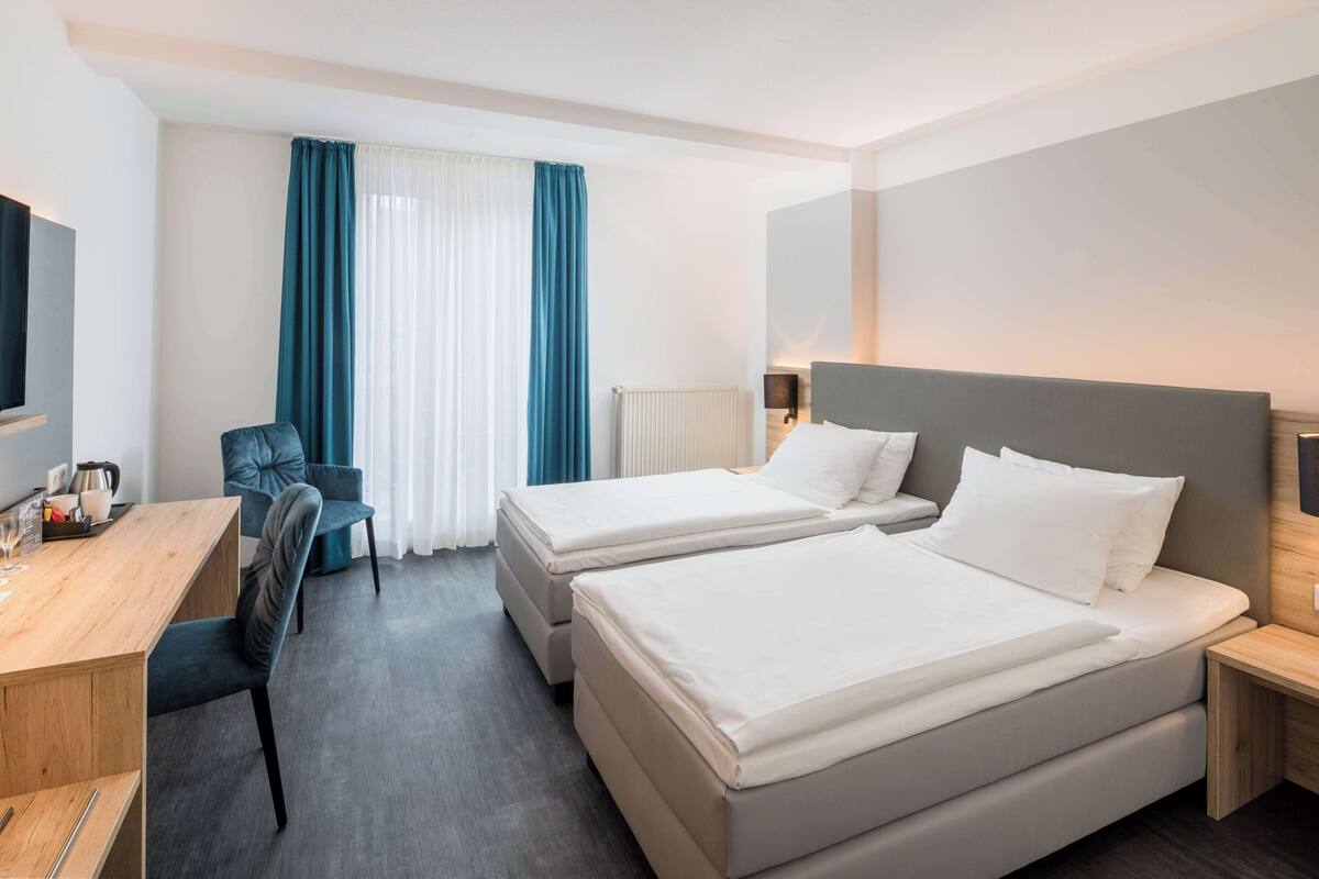 A hotel room with two beds, a desk, a chair, and a TV.