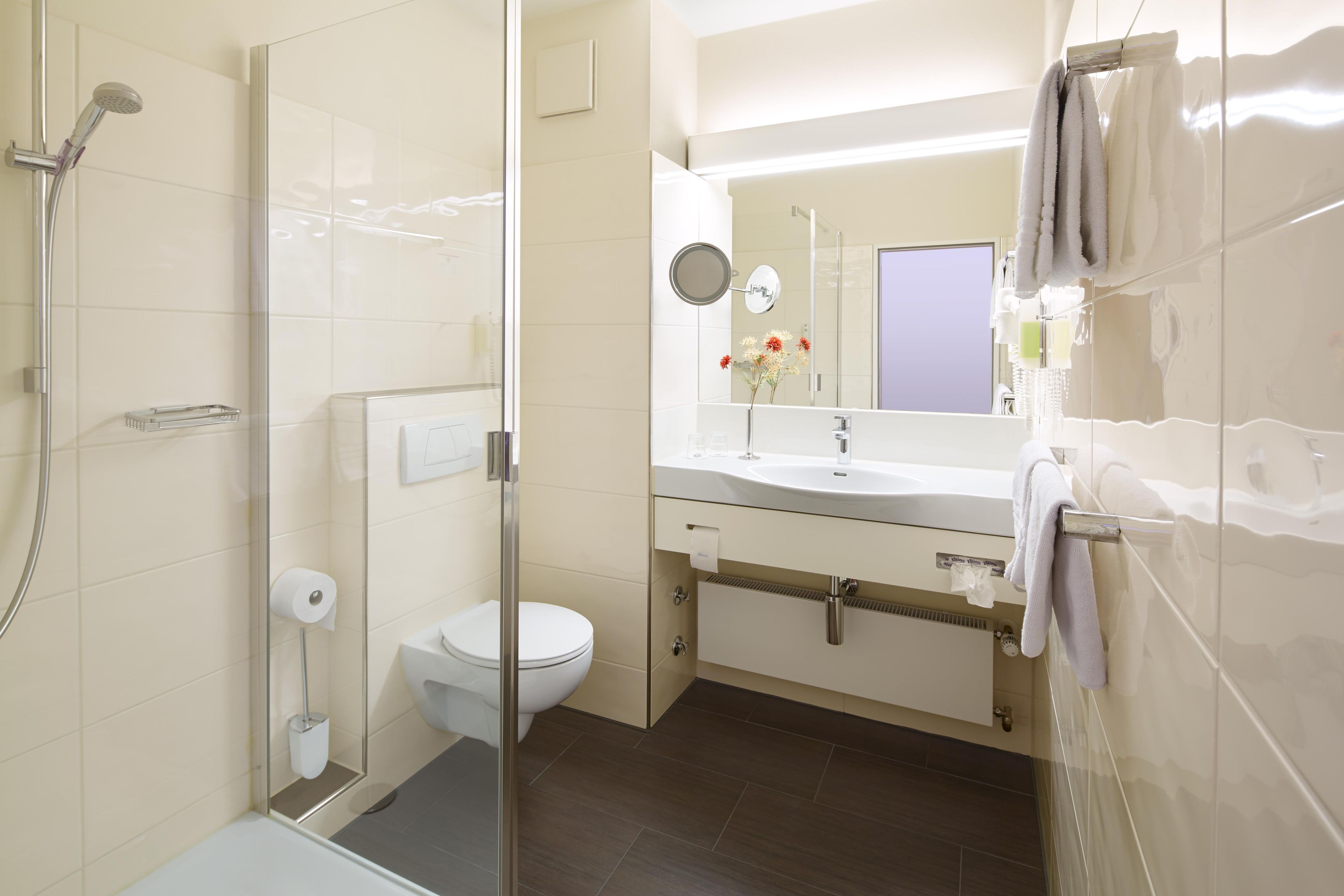 A modern bathroom with a glass shower enclosure, a toilet, a sink with a mirror, and a towel rack.