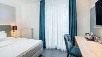 Una habitació d'hotel amb un llit, una taula de treball, una cadira, un televisor i una finestra amb cortines.