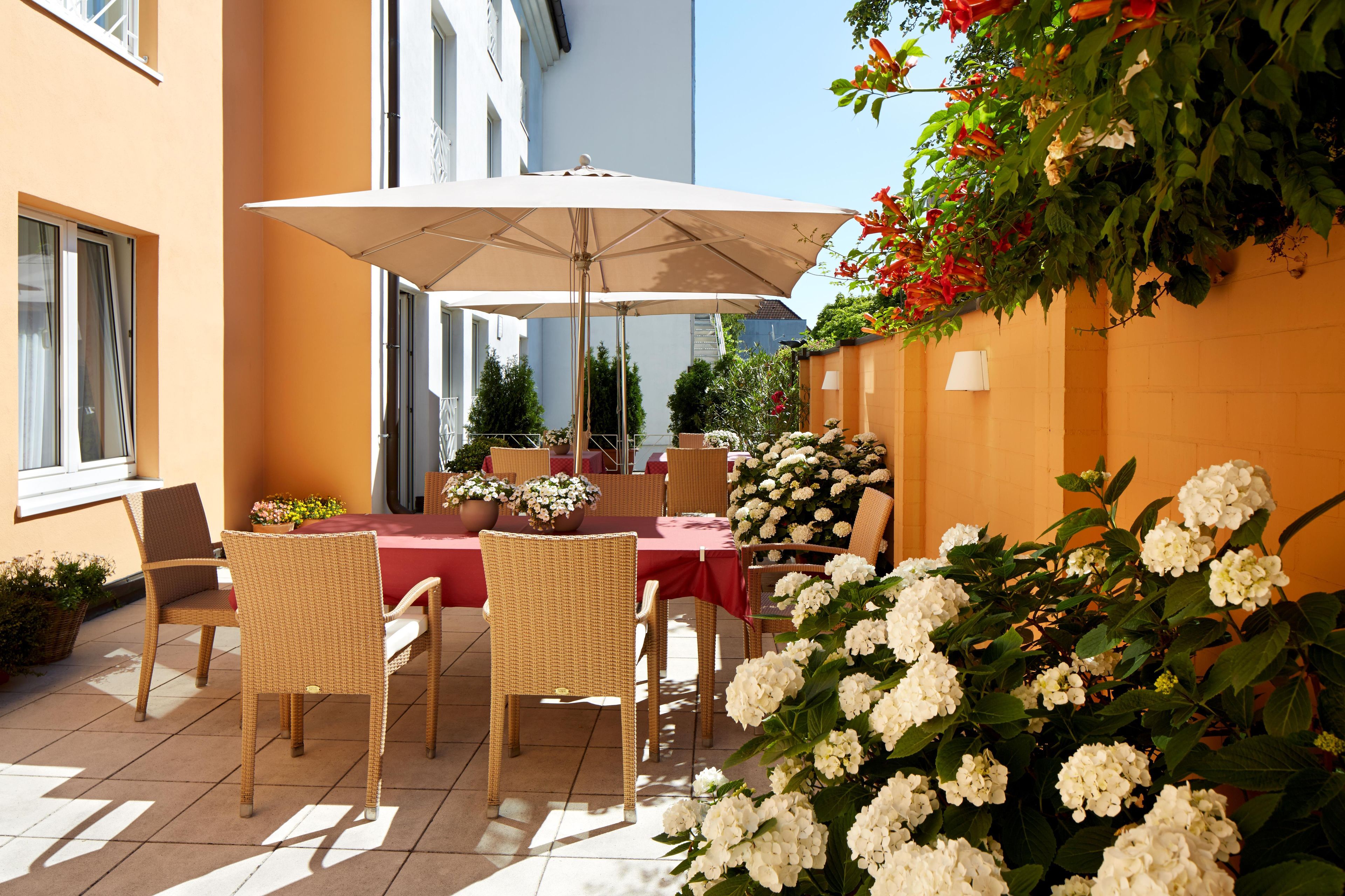 An outdoor patio with a table and chairs, a large umbrella, and potted plants.