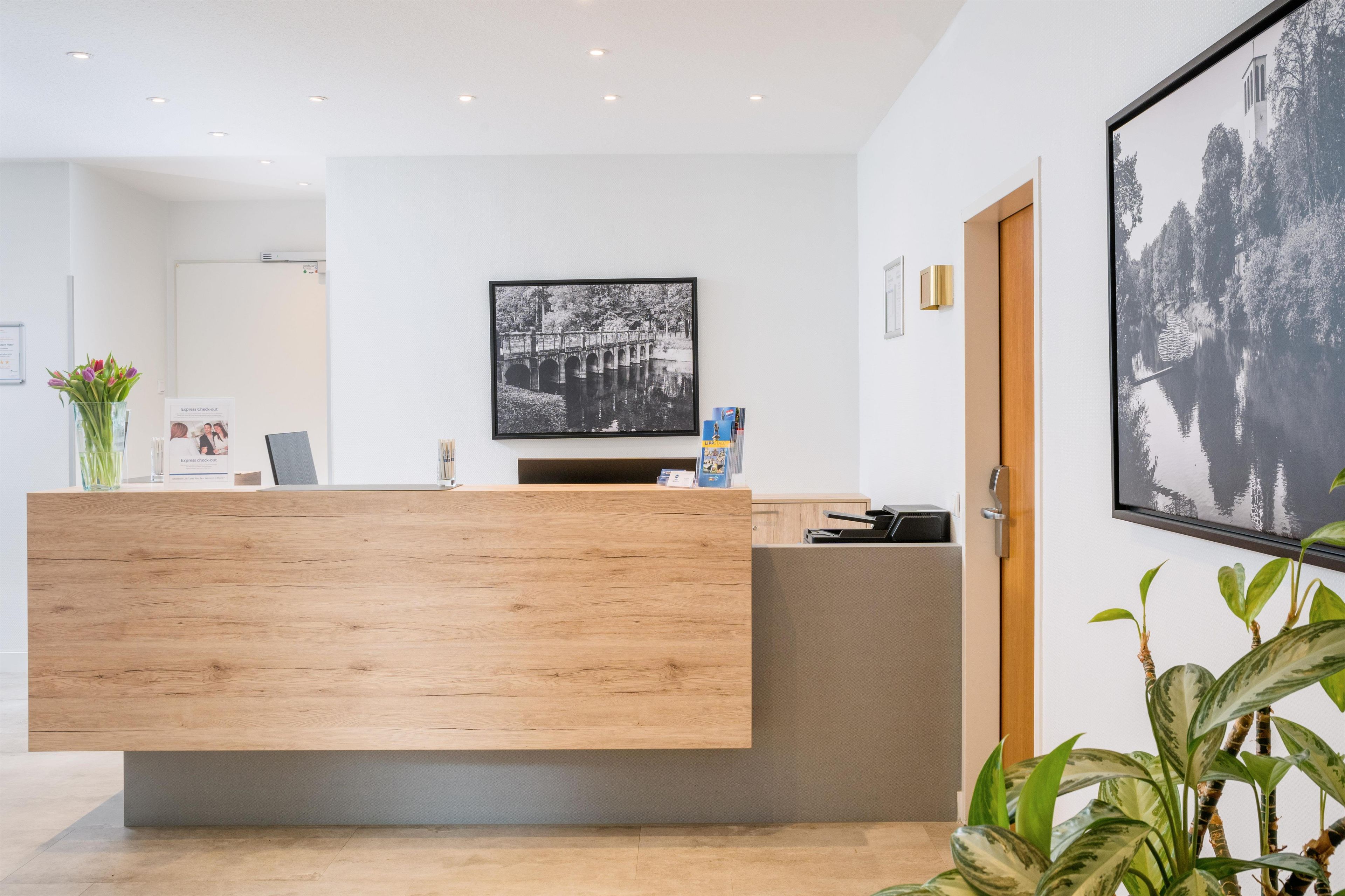 A reception desk with a wooden finish, a black and white photograph on the wall, and a door to the right.