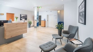 A modern reception area with a wooden desk, grey seating, and potted plants. - Best Western Hotel Lippstadt (Lippstadt)