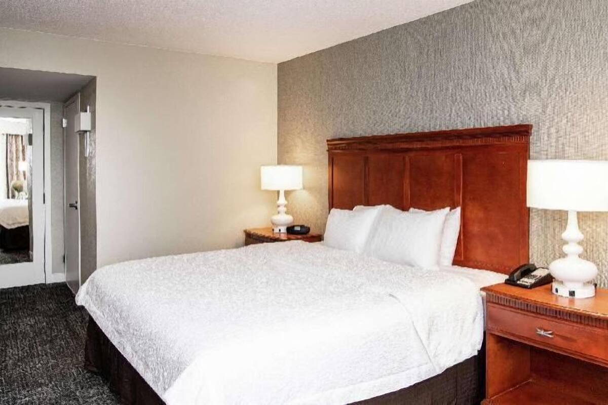 A hotel room with a large bed, two bedside tables with lamps, a wooden headboard, and a carpeted floor.