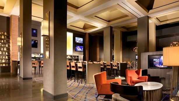 A modern hotel lobby with a bar area, seating, and a television screen.