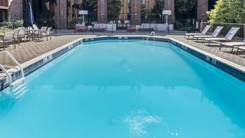 A rectangular swimming pool with a tiled edge, surrounded by lounge chairs and a brick building in the background.