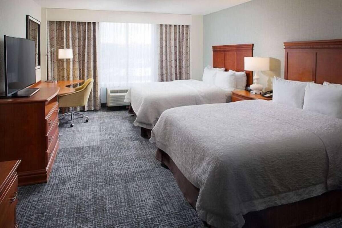 A hotel room with two beds, a desk with a chair, a television, and a window with curtains.
