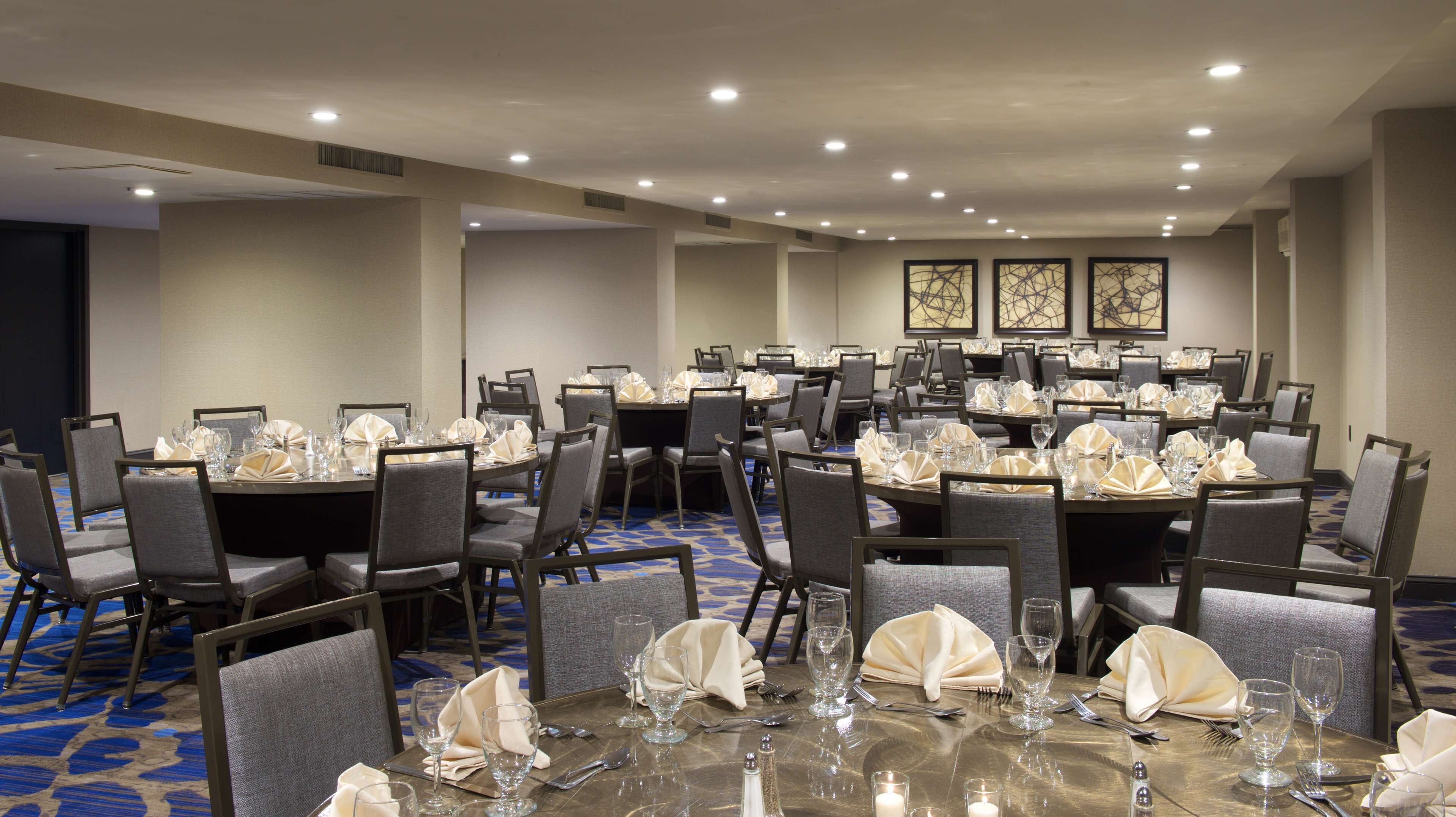 A conference room with round tables, grey chairs, and white tablecloths.