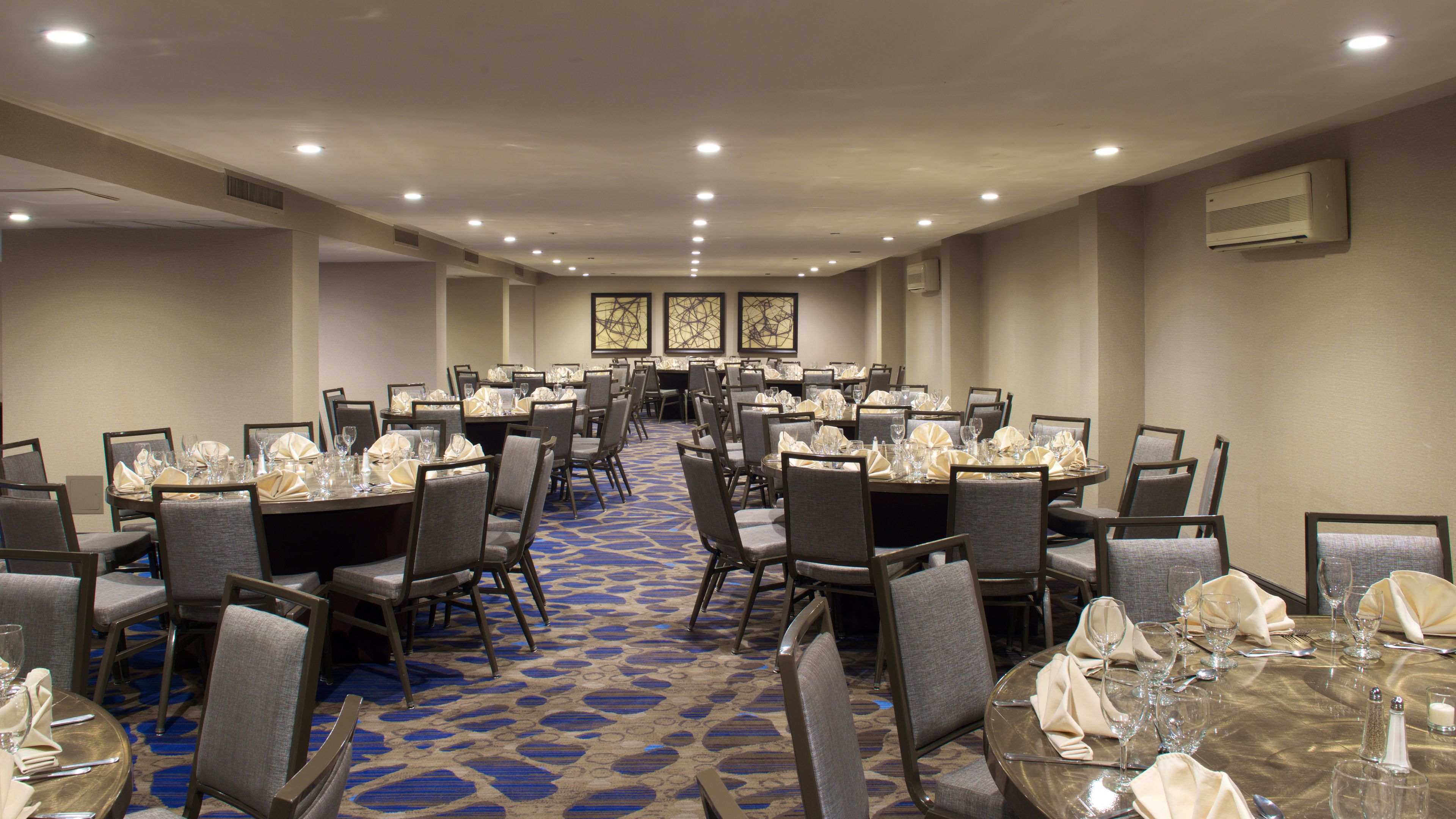 A conference room with multiple tables set for dining, equipped with chairs and tables, and a patterned carpet.