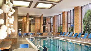 A modern indoor pool area with blue lounge chairs, a pool table, and a brick wall.