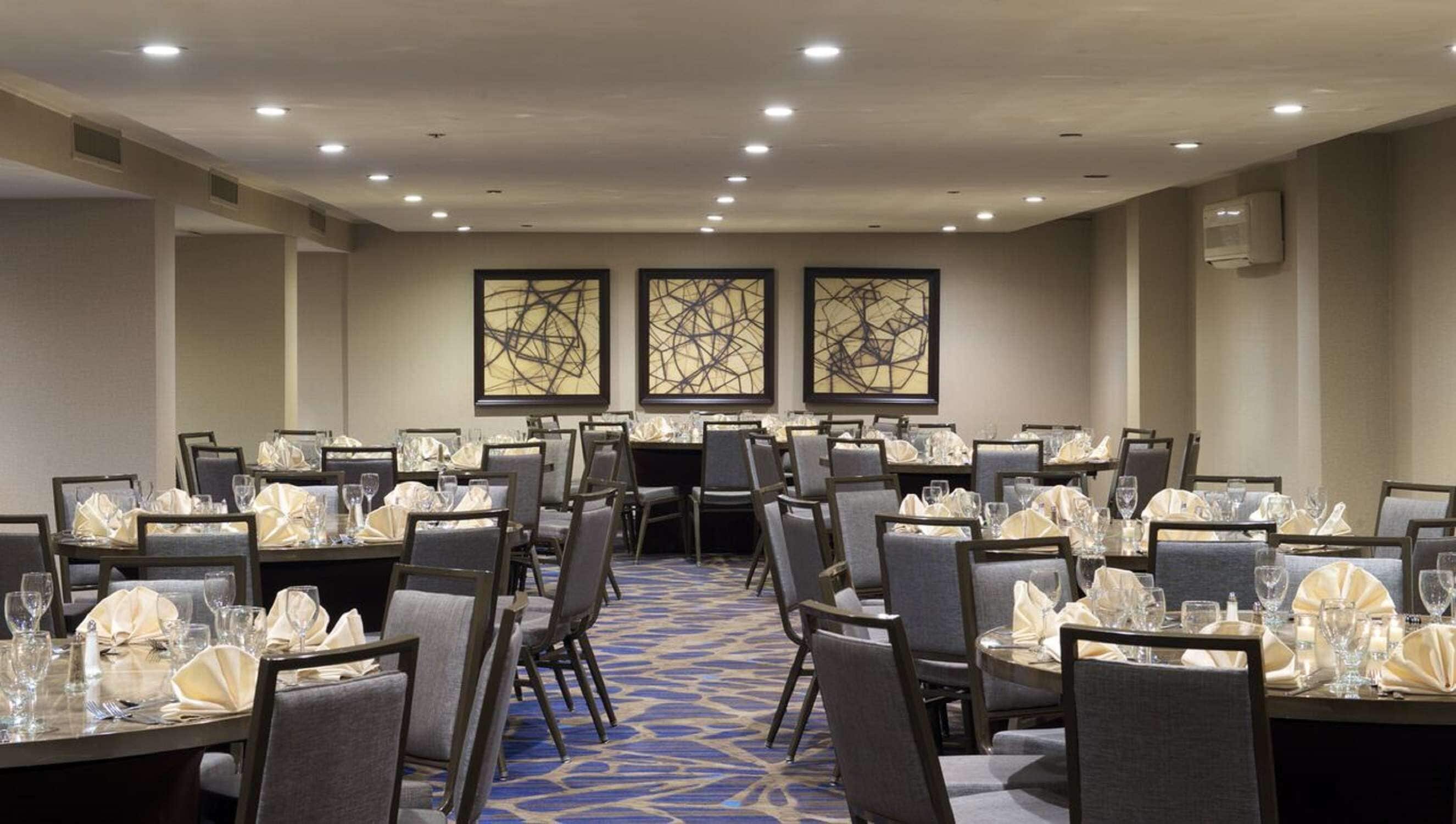 A conference room with round tables, grey chairs, and a blue patterned carpet.