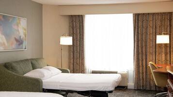 A hotel room with a bed, a desk, a chair, two lamps, and a painting on the wall.