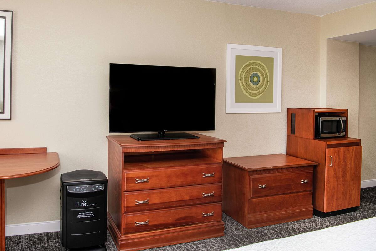 A hotel room with a flat-screen TV, a wooden dresser, a desk, and a microwave.