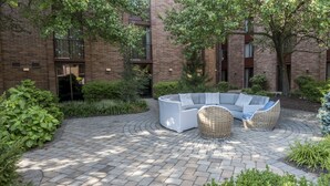 A courtyard with a curved white sofa and wicker chairs, surrounded by brick buildings and greenery.