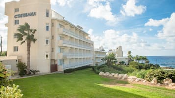A multi-story hotel with a name sign, a well-maintained lawn, and a view of the ocean.