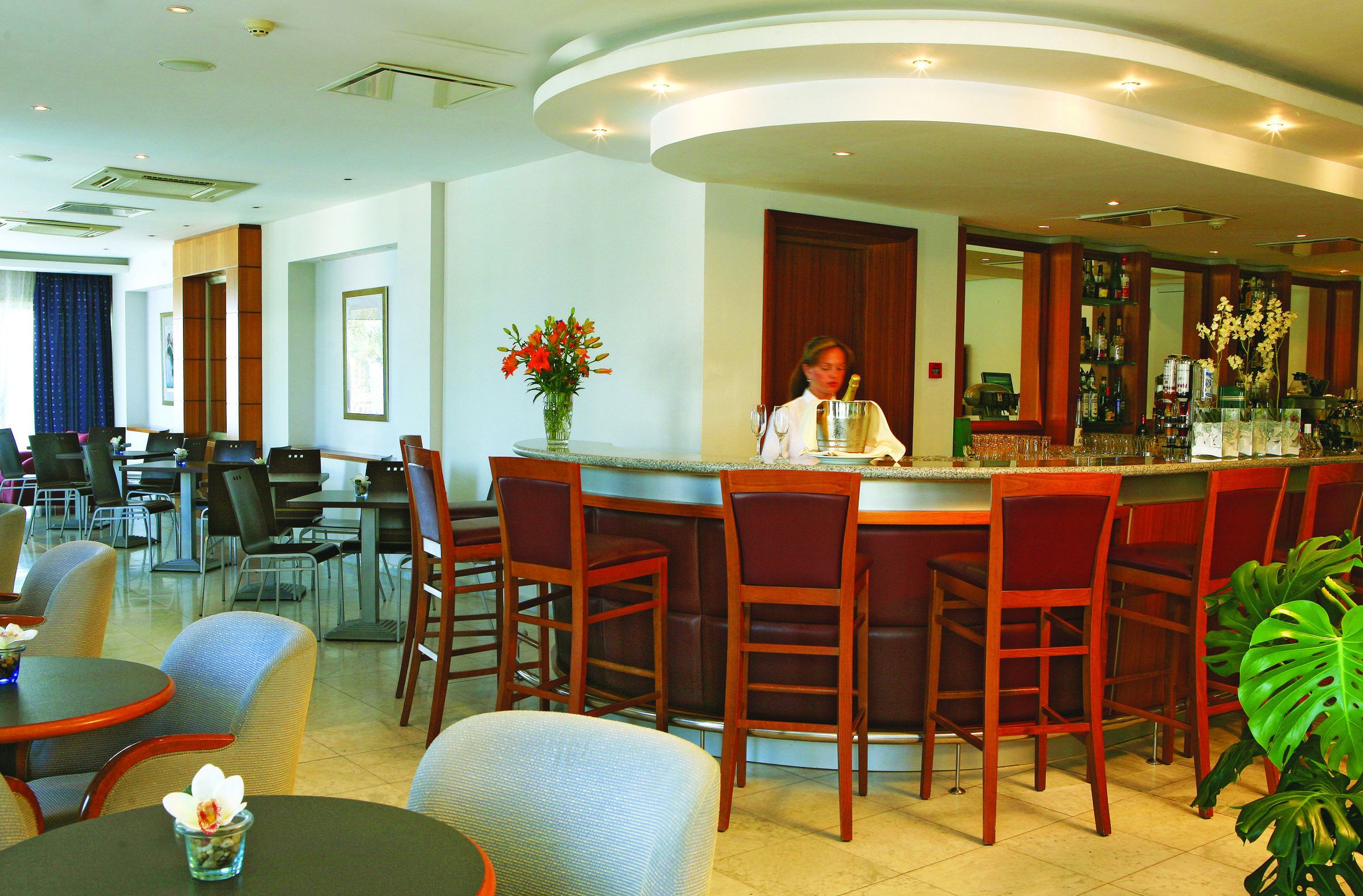 Un bar de hotel con sillas de madera, una barra y una mujer sirviendo.