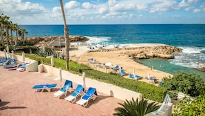 Um resort à beira-mar com espreguiçadeiras e guarda-sóis, costa rochosa e céu azul límpido.