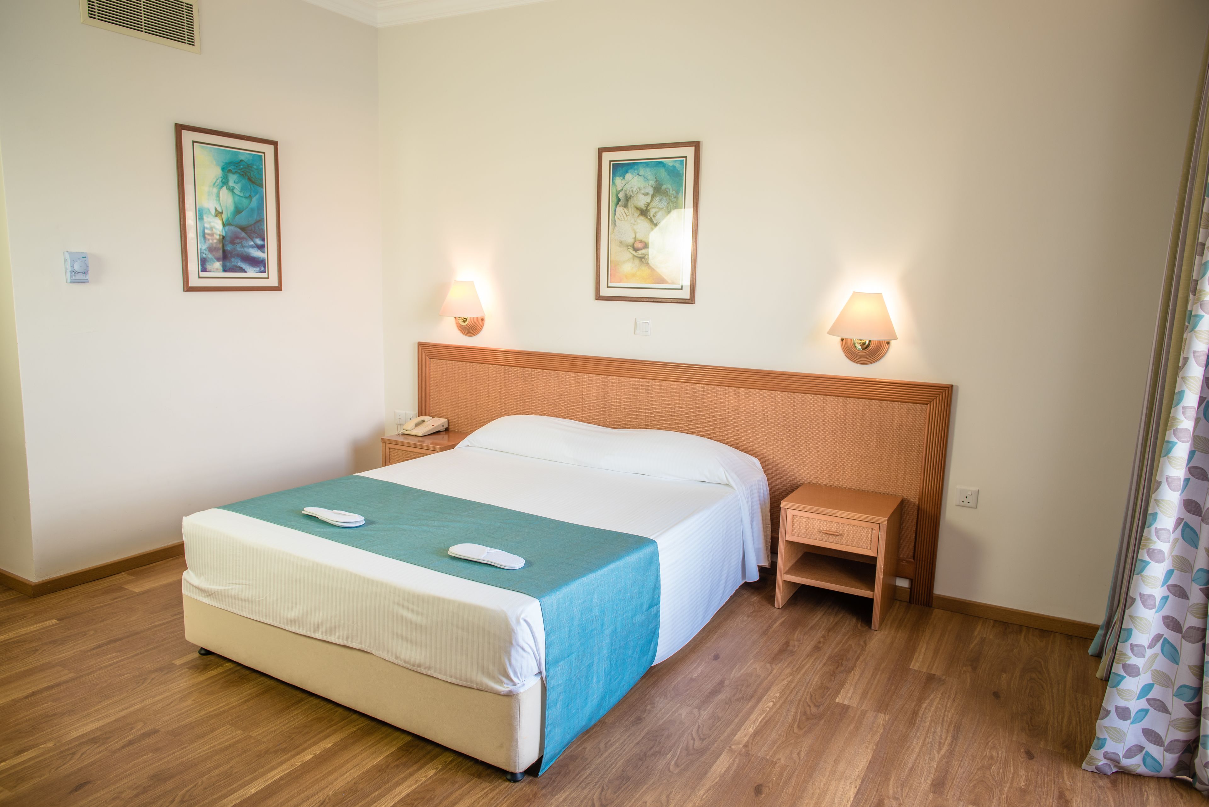 Une chambre d’hôtel avec un grand lit, deux tables de chevet, une petite table et deux lampes fixées au mur.
