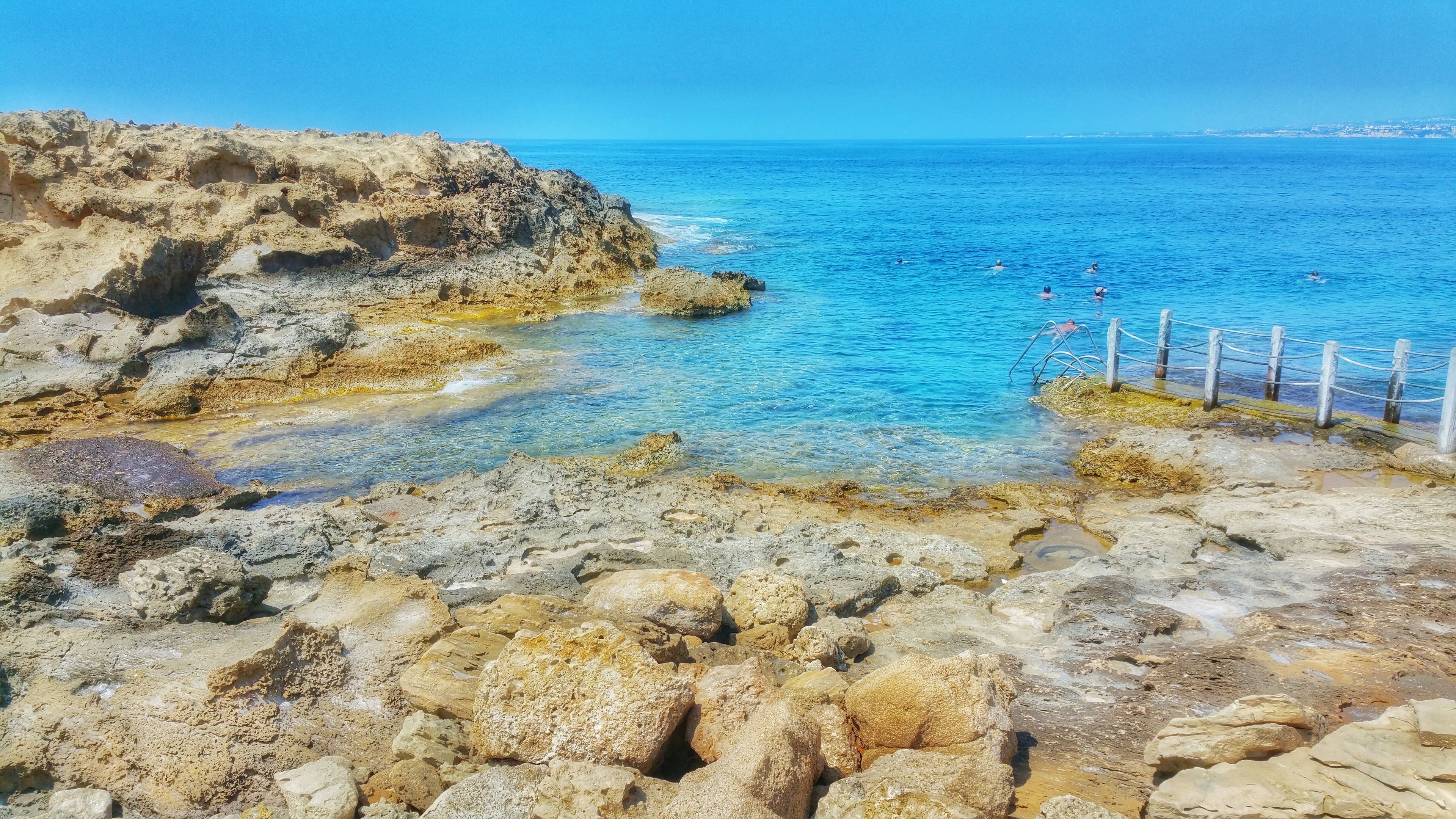 A rocky coastline with clear blue waters and a wooden fence.