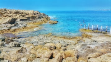 A rocky coastline with clear blue waters and a wooden fence.