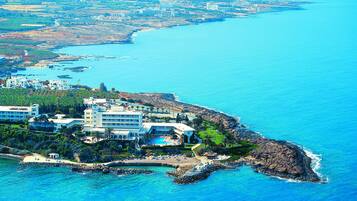 An aerial view of a coastal resort with multiple buildings, a beach, and a clear blue sea.