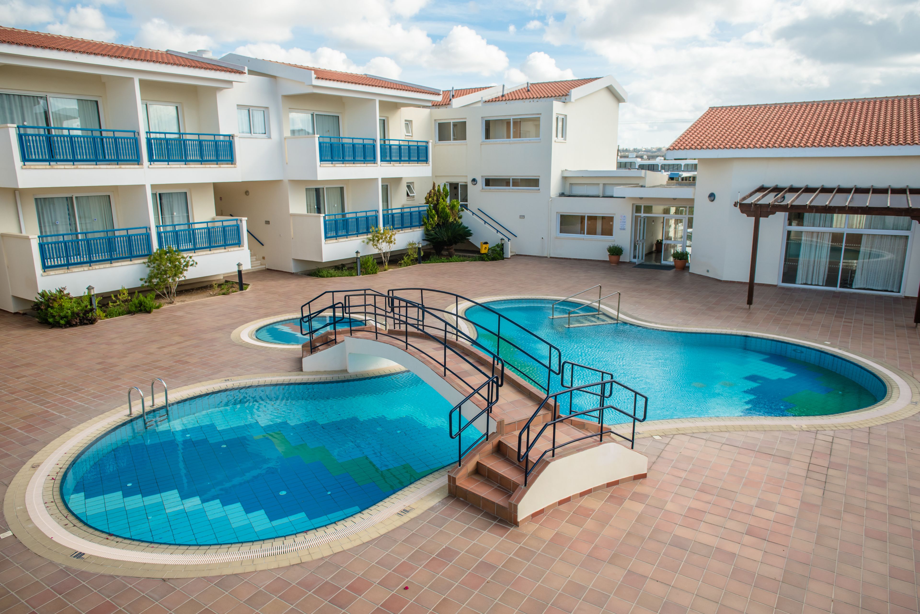 Una piscina rodeada de edificios de varios pisos con balcones, un área de patio techada y un cielo despejado.