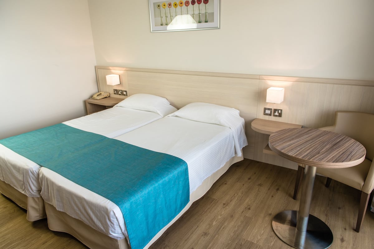 A hotel room with a bed, bedside tables, a round table, and a wall-mounted lamp.